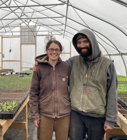 Two farmers smiling in a greenhouse with seedlings.