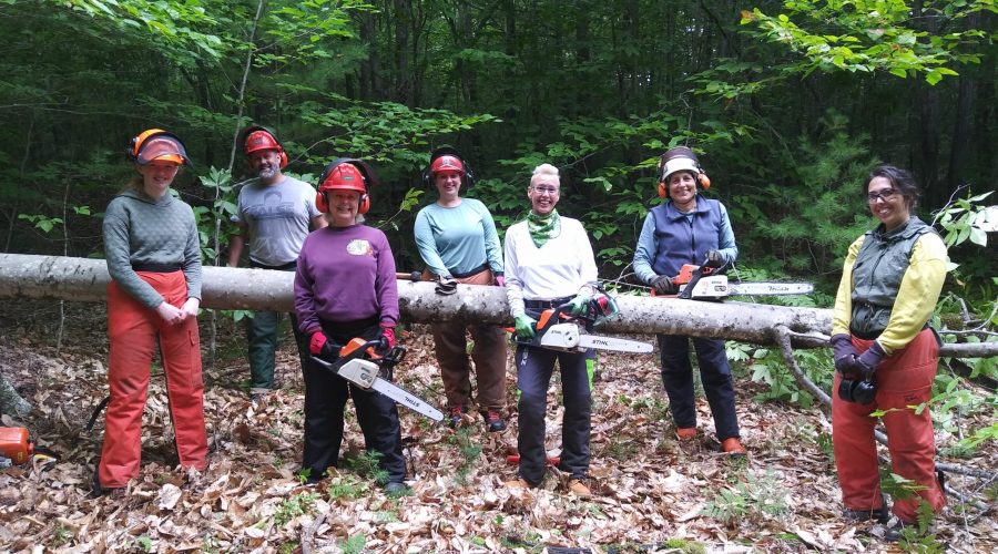 A group of people smiling while holding logs and chainsaws.