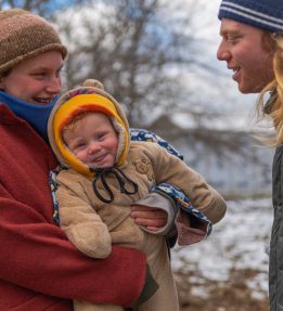 Couple in knit hats holding baby in winter field.